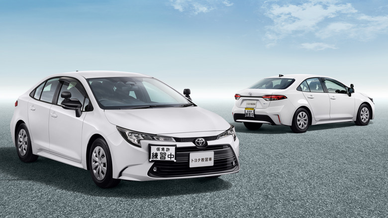 Two basic white Toyota Corolla Japanese driving school models pictured next to each other with a sky blue background.