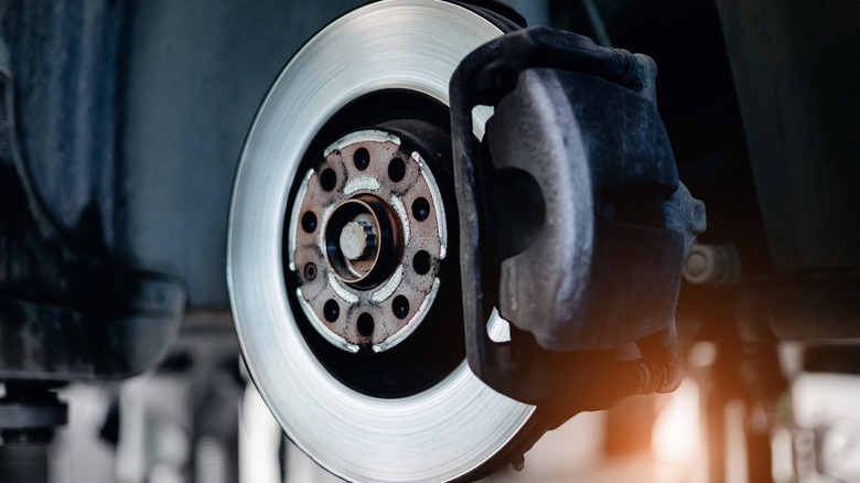 A vehicle's brake disc and caliper setup up close, sunset in the background