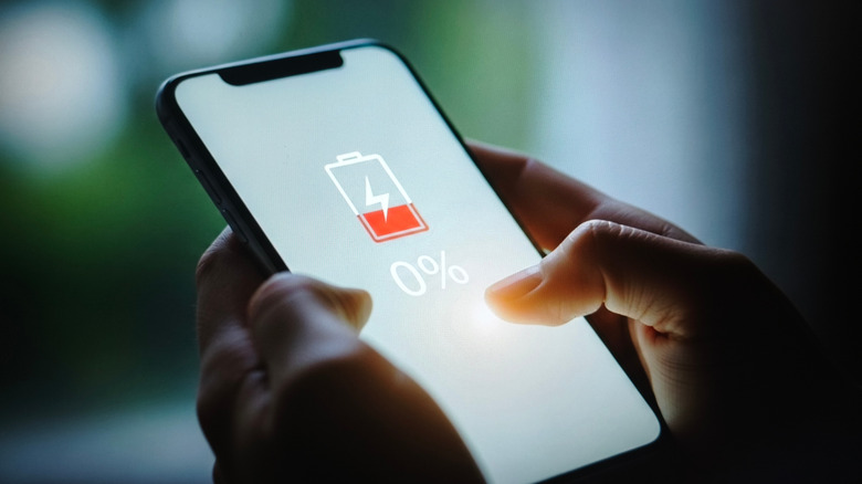 Person holding a smartphone with an on-screen indicator showing an empty battery