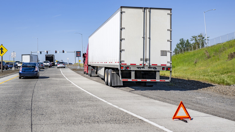 White and red semi-truck pulled over on the road with orange hazard triangle in rear