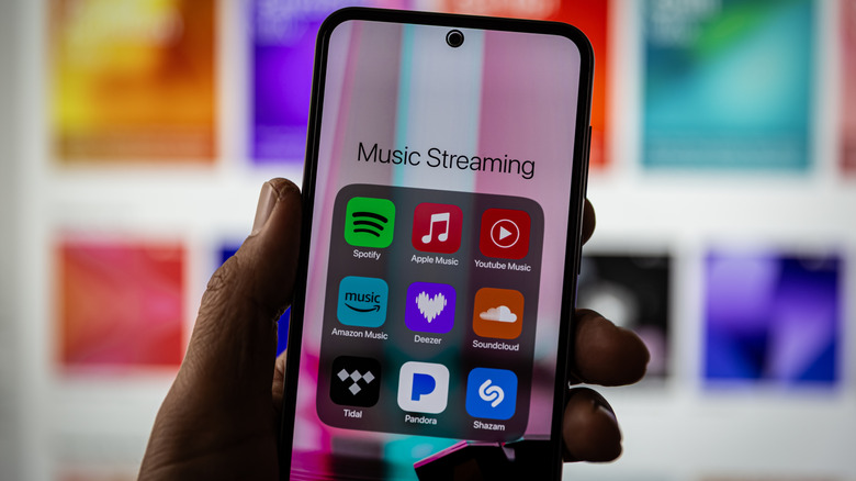 Someone holding an iPhone showing music streaming apps.