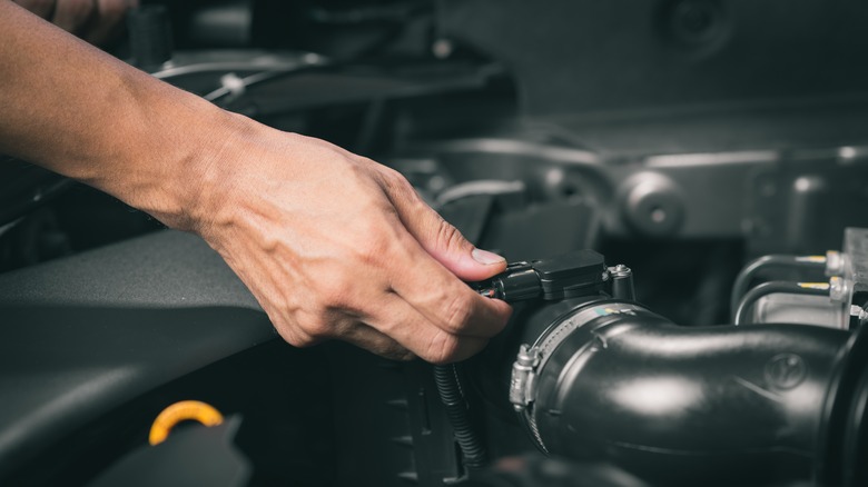 A persons hand reaching into an engine bay in the process of disconnecting the mass air filter sensor.