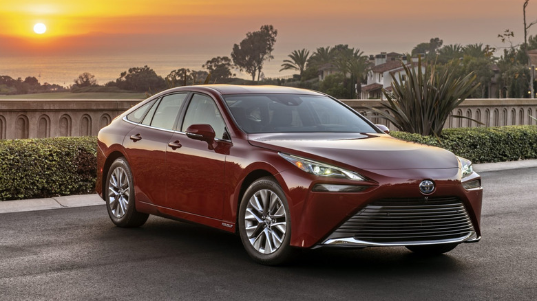 Front 3/4 view of red 2023 Toyota Mirai parked on a suburban street at sunset.