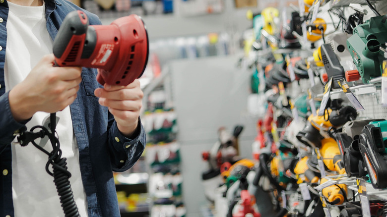Man holding power tool in aisle with multiple power tool brands to choose from