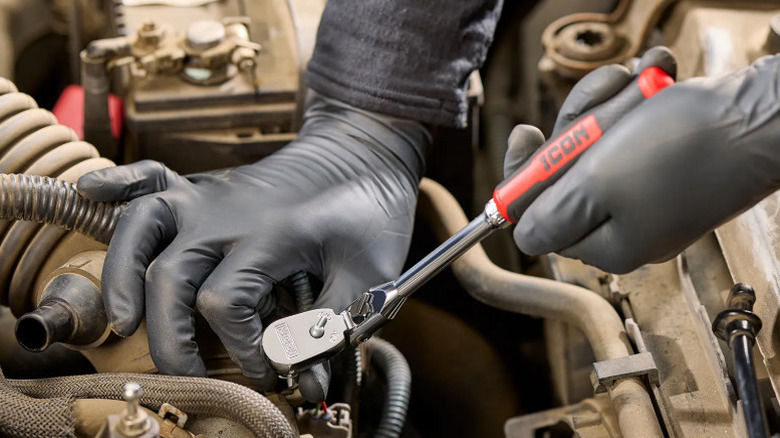 A pair of gloved hands working on a car with a Harbor Freight icon ratchet.