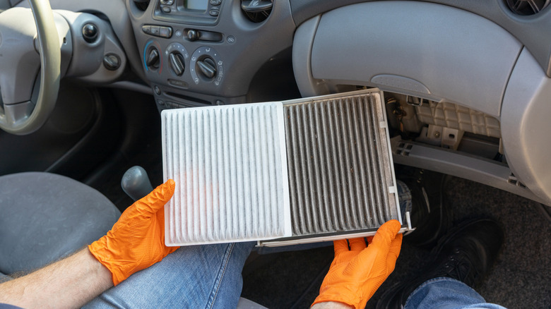 Person holding two cabin air filters in the front seat of a vehicle.