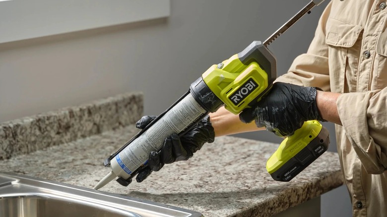 A person using a Ryobi Caulk Gun on a kitchen sink.