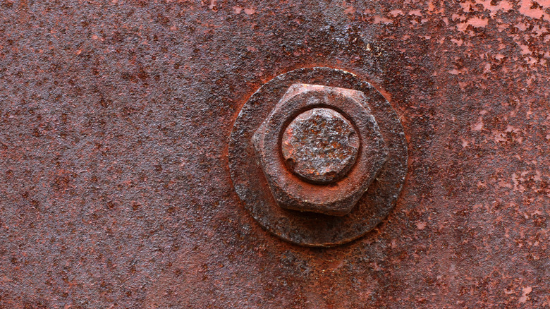 A rusty nut and bolt on a metal plate