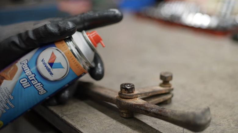 A man sprays a rusted nut with penetrating oil
