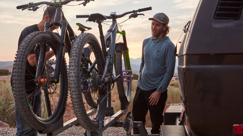 Two people unloading mountain bikes from a hitch-mounted bike rack