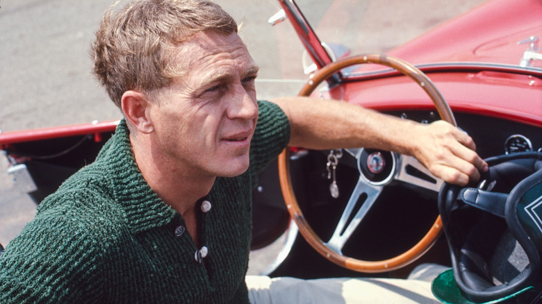 Steve McQueen inside a red convertible vehicle with wooden steering wheel