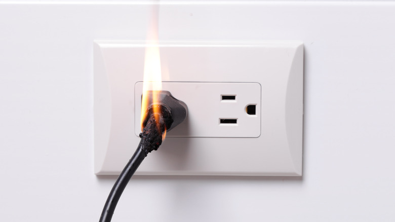 black cord and plug on fire in an electrical outlet