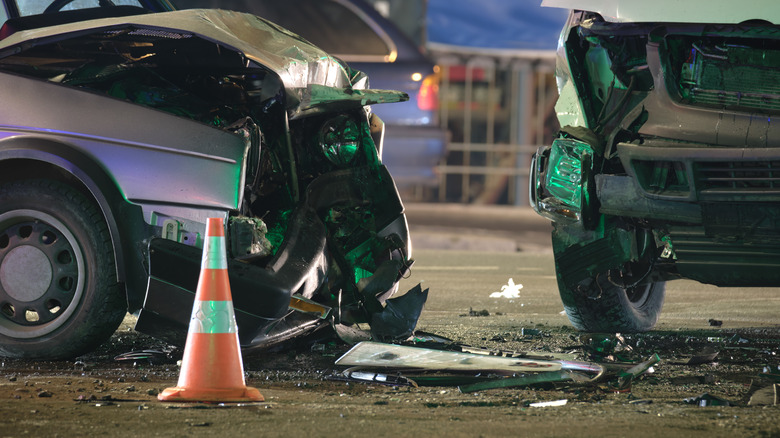 Close-up of two vehicles heavily damaged from a collision, with a traffic cone in the foreground