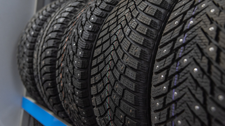 A row of black studded car rubber tires on shelf in a shop for winter