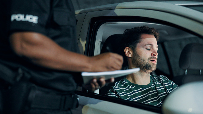 Police officer writing a citation for a driver sitting inside a vehicle