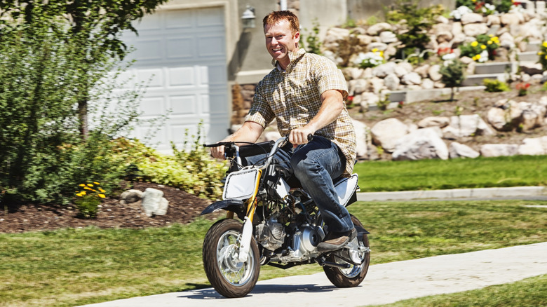 Photo of a man riding a miniature dirt bike on a neighborhood sidewalk