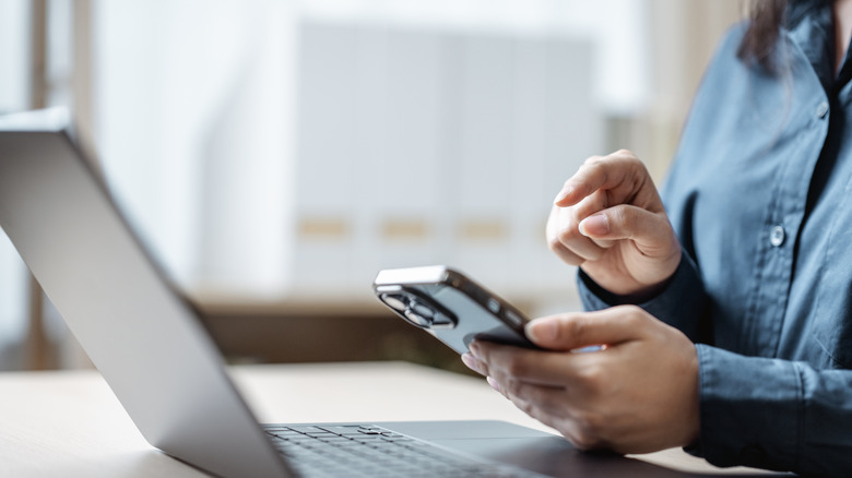Person using a smartphone while sitting in front of a laptop