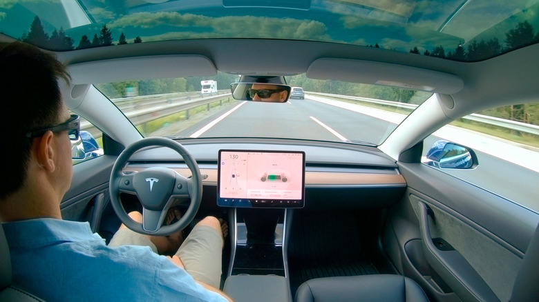 Man sits with hands off wheel in FSD mode in a Tesla on the highway