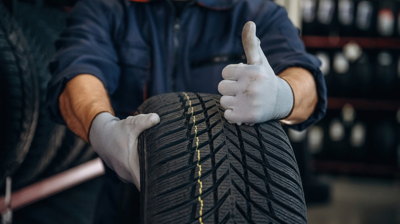 Tire technician in tire store holding tire and giving thumbs up sign