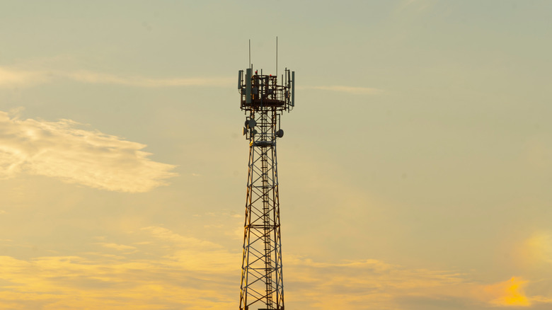 A cell phone tower against a cloudy sky at sunset