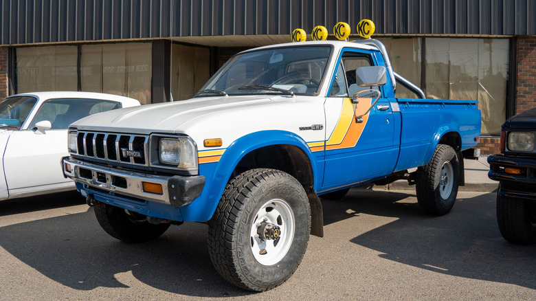 Front 3/4 view of white and blue Toyota 4x4 pickup parked at car show.