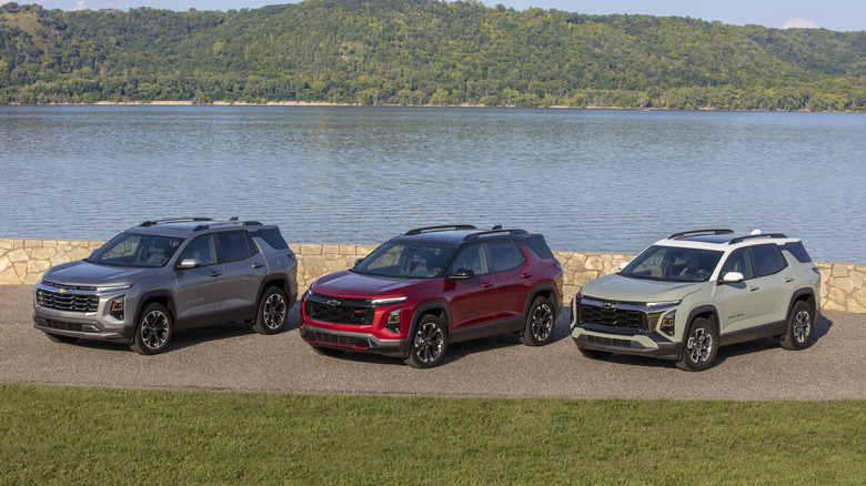 A trio of Chevrolet Equinox SUVs by a lake, one gray, one red, and one green