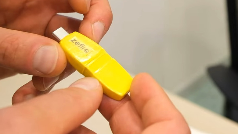 A close up of the Zefiro dongle in orange held between two hands.