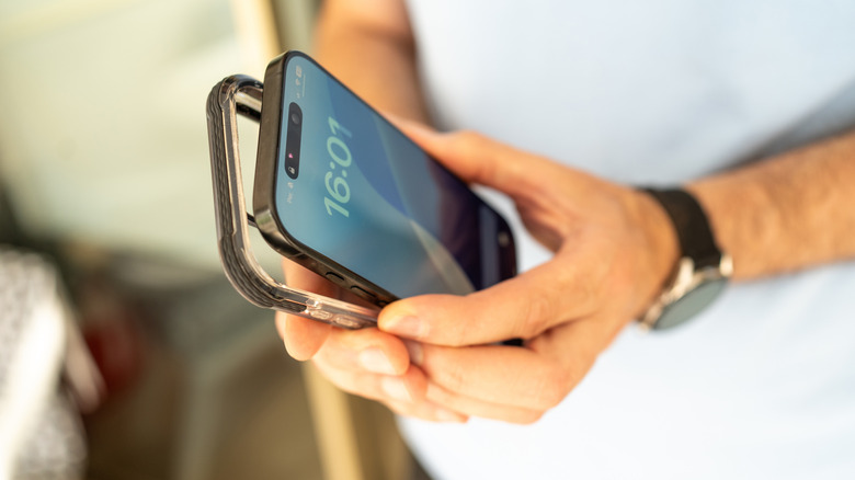 Close-up of a person holding a smartphone and a transparent protective case, preparing to put the case on the phone.