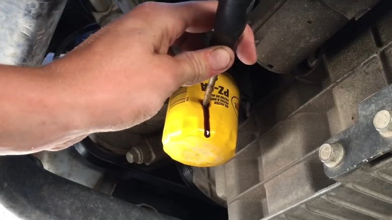 A person hammering a screwdriver into their stuck oil filter