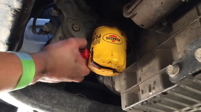 A person using a screwdriver to remove a stuck oil filter