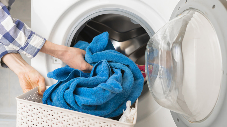 Person loading a blue towel into a washing machine