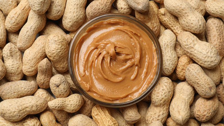 A jar of peanut butter surrounded by peanuts