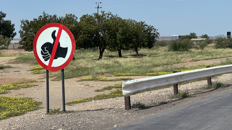 No hitchhiking sign next to the road in Africa. This one looks very similar to the one used in the United States.