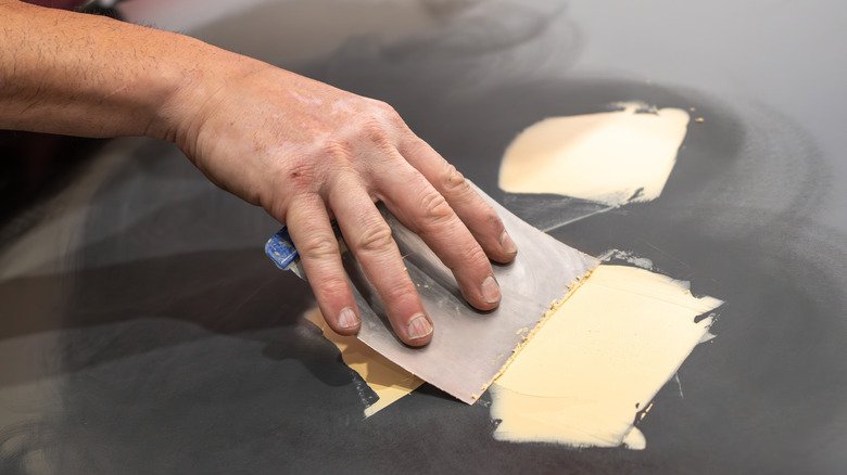 A person applies body filler to a car hood