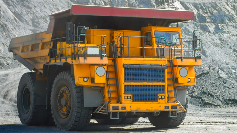 A yellow BelAZ 75710 dump trucks driving around an ore quarry, front 3/4 view