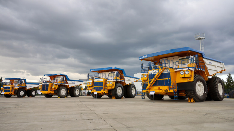 A lineup of BelAZ dump trucks in yellow, white, and blue color schemes