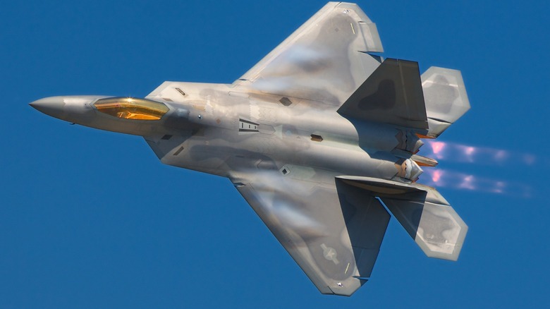 A Lockheed Martin F-22A Raptor with its afterburners engaged over a blue sky