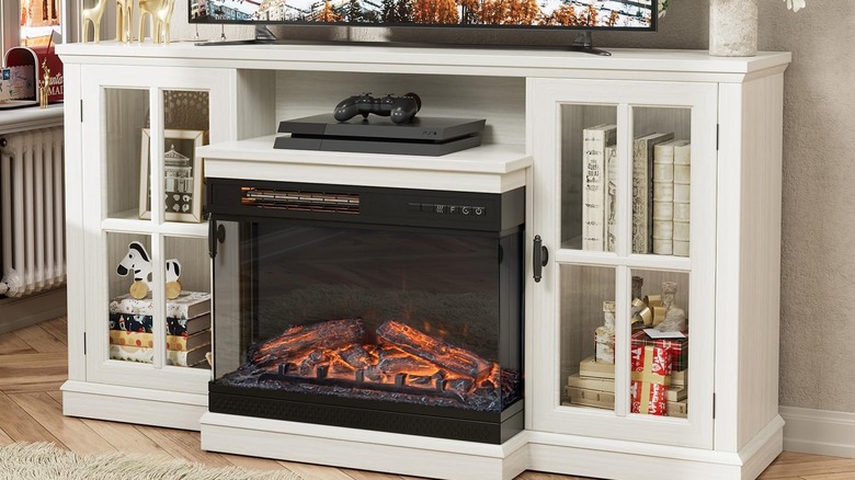 A TV stand wit an electric fireplace that has books and a PS4 console and controller inside.