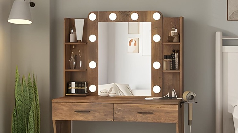 A vanity with its lights turned on and makeup products inside, a hairdryer is plugged into the built in outlets.