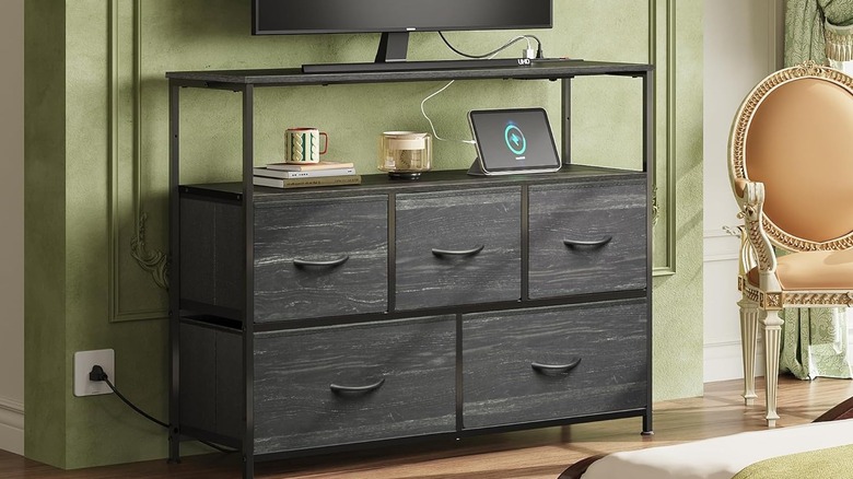 A dresser that is plugged in with a tablet charging next to some books under a TV.