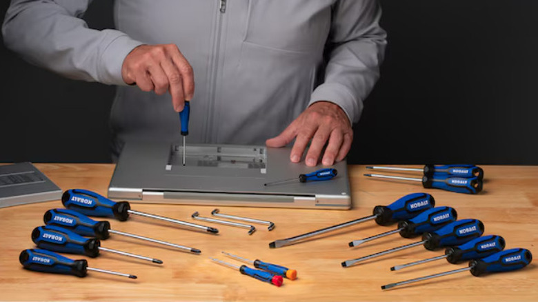 Screwers used on the back of a laptop with multiple spread out on a wooden table