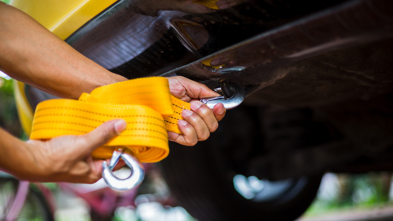 A person attaches a tow strap to a car