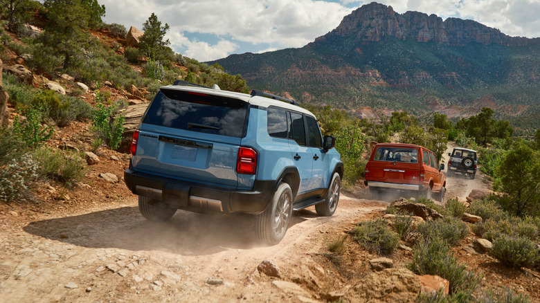 A 250 Toyota Land Cruiser in blue with a white roof off-roading with two old Land Cruisers