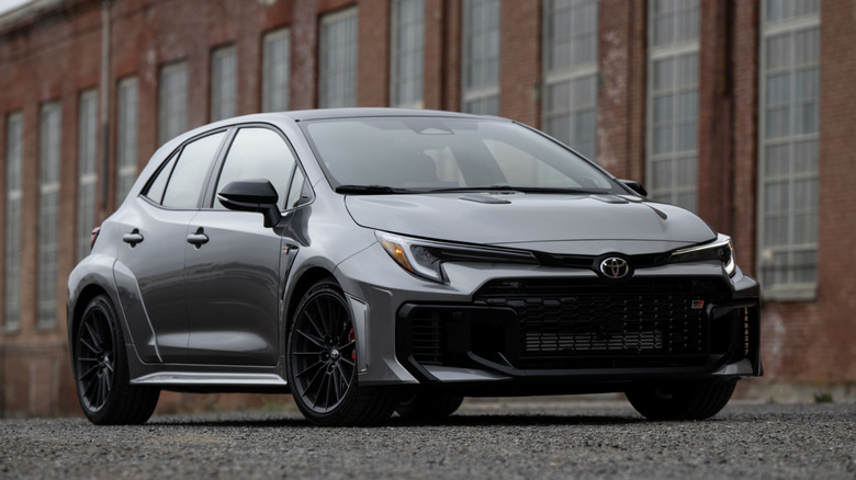 Front 3/4 view of gray 2026 Toyota GR Corolla parked in front of building.