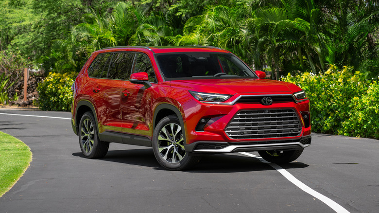 Ruby Flare Pearl 2025 Toyota Grand Highlander Platinum parked on a road with trees in the background