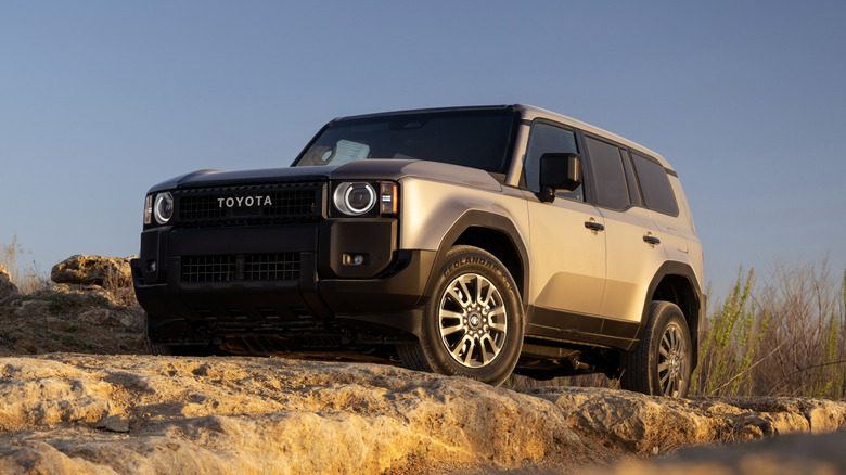 Base-model 2026 Toyota Land Cruiser 1958 on a rock formation, front 3/4 view, silver exterior, round headlights