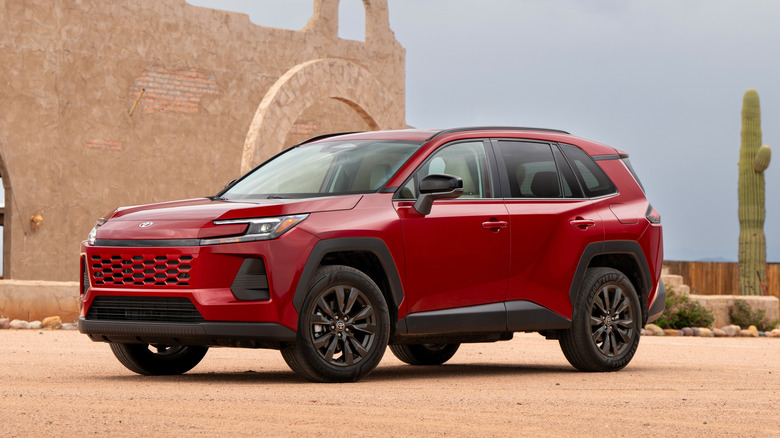 A red 2026 Toyota RAV4 parked on a dirt road with a brick building and a cactus in the background
