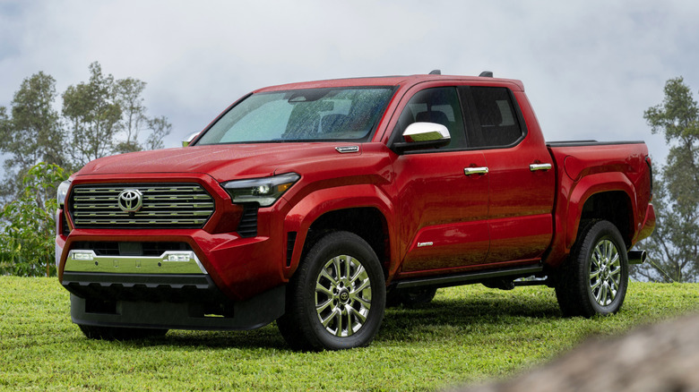 A bright red 2026 Toyota Tacoma parked on grass on a cloudy day