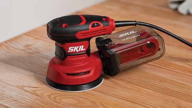 A Skil random orbit sander sitting on wooden surface.