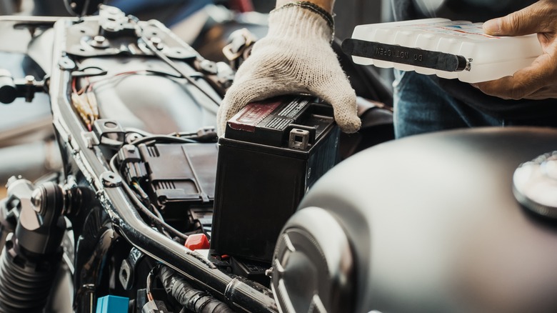 Hands installing a motorcycle battery.